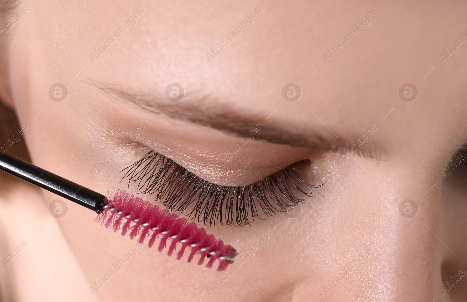 Photo of Attractive young woman applying mascara on her eyelashes, closeup