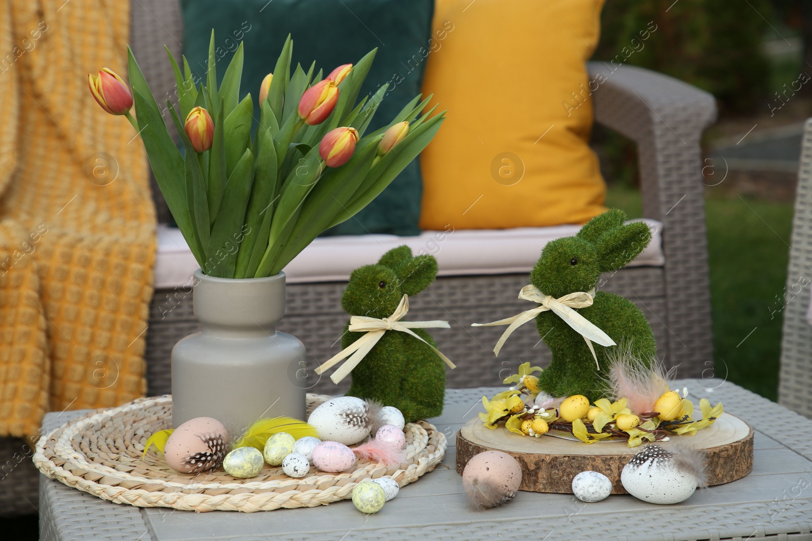 Photo of Terrace with Easter decorations. Bouquet of tulips in vase, bunny figures and decorative eggs on table outdoors