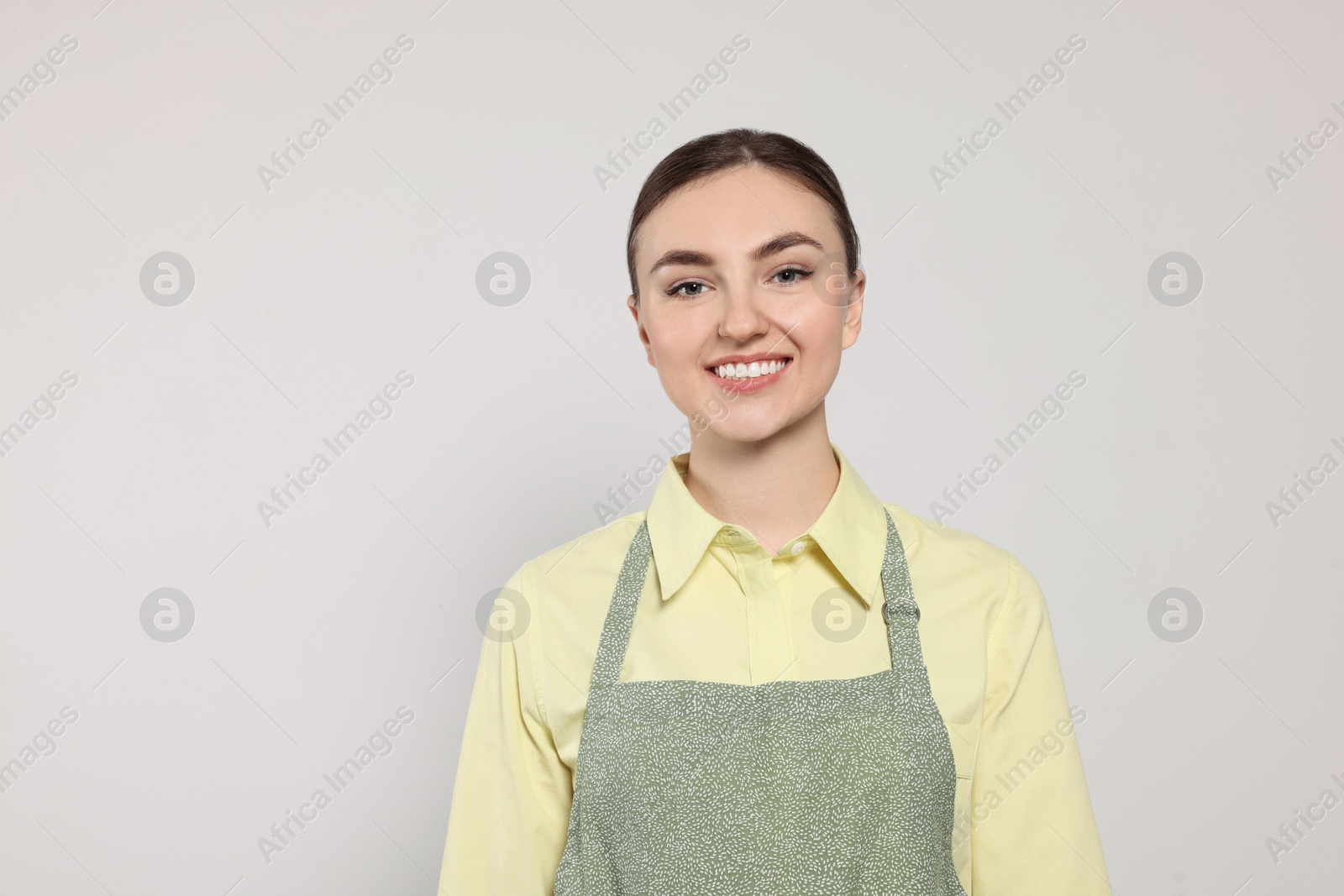 Photo of Beautiful young woman in clean apron with pattern on light grey background