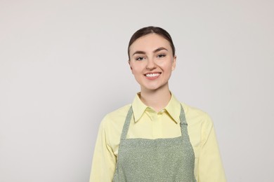 Beautiful young woman in clean apron with pattern on light grey background