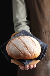 Photo of Woman holding freshly baked bread on black background, closeup