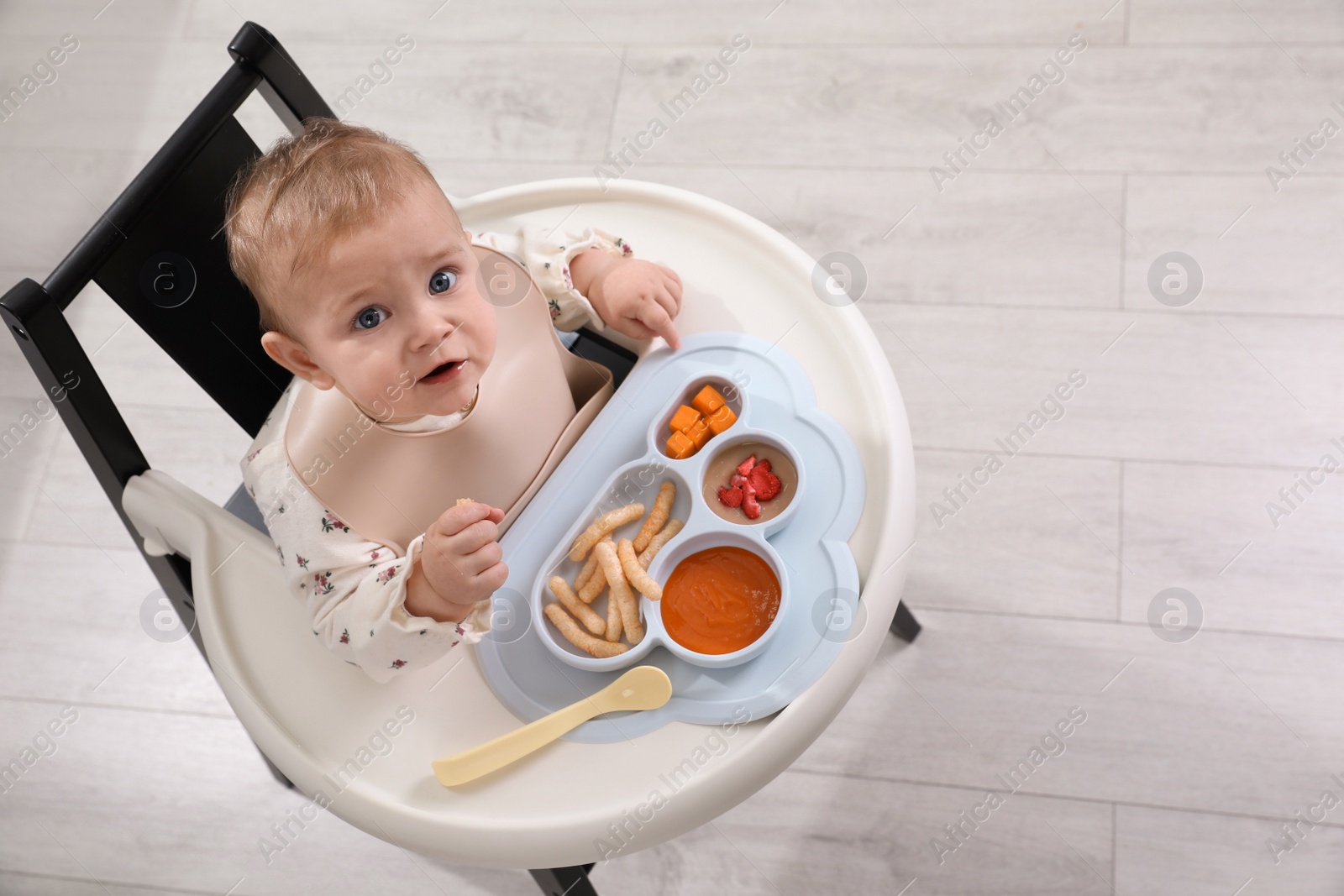 Photo of Cute little baby eating food in high chair indoors, above view. Space for text