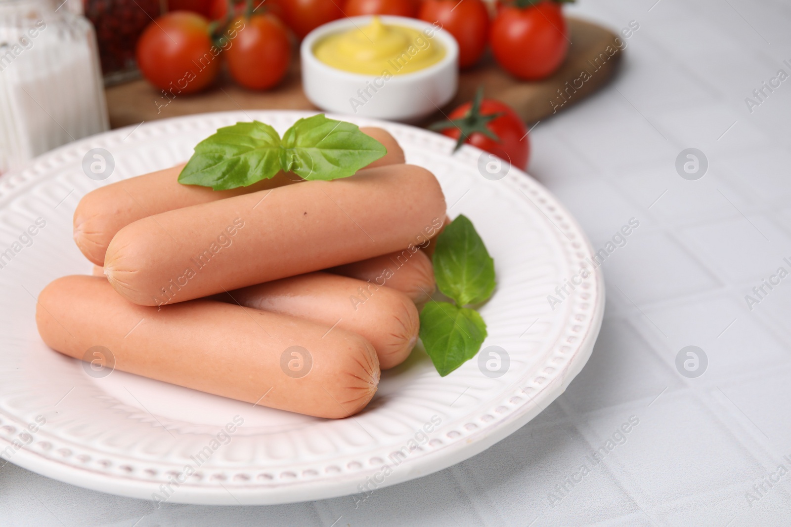 Photo of Delicious boiled sausages and basil on white tiled table, closeup