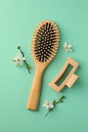 Photo of Wooden hairbrush, flower branches and barrette on turquoise background, flat lay