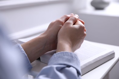 Photo of Religion. Christian woman praying over Bible indoors, closeup