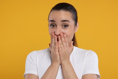Photo of Embarrassed woman covering mouth with hands on orange background