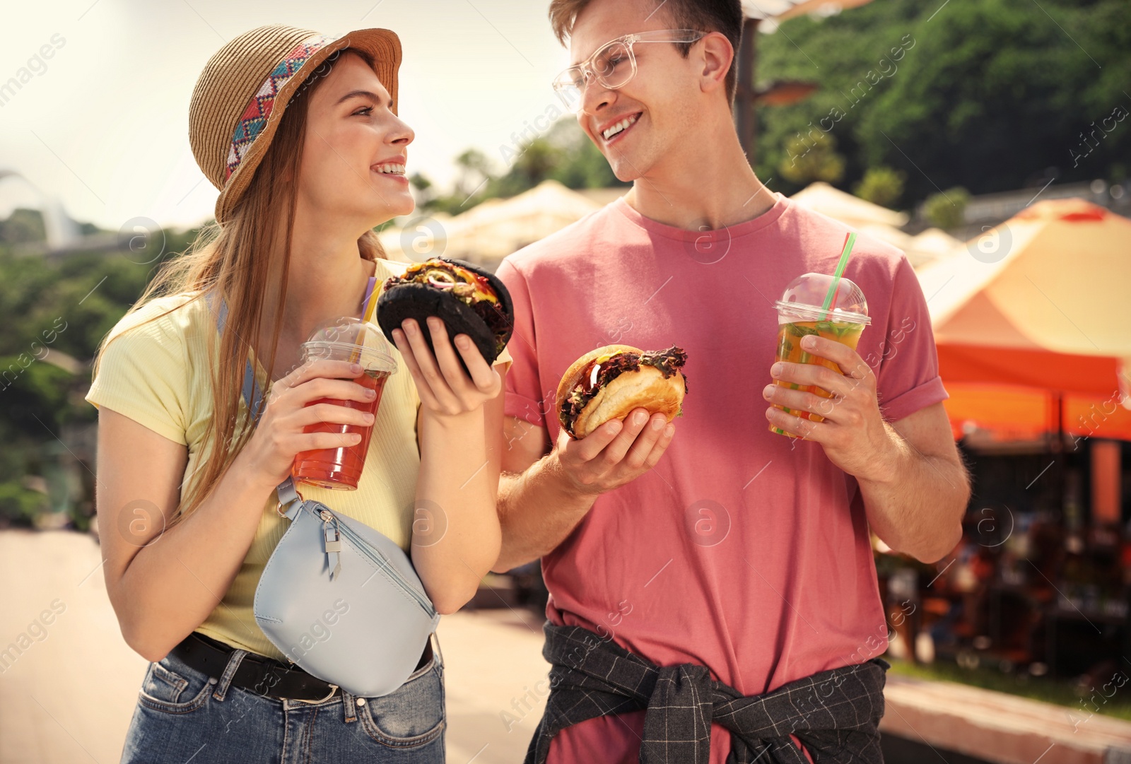 Photo of Young happy couple with burgers walking on city street