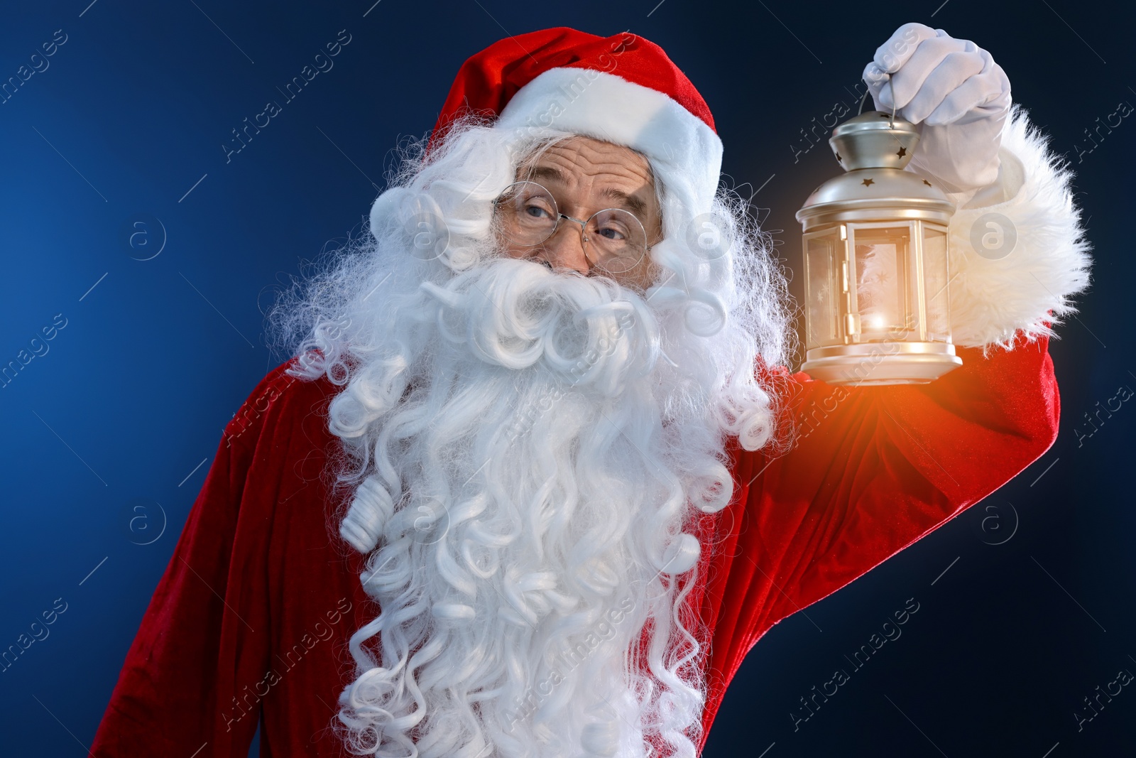 Photo of Santa Claus holding Christmas lantern with burning candle on dark blue background