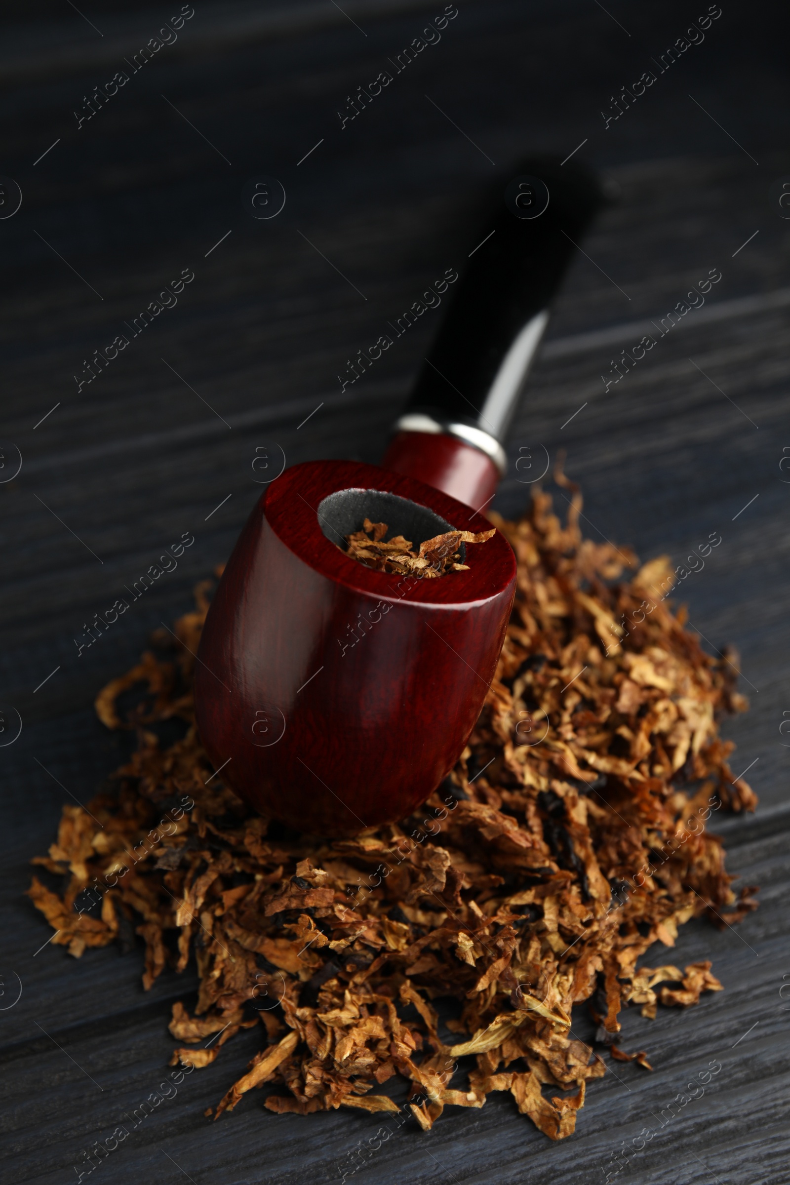 Photo of Smoking pipe and dry tobacco on black wooden table, closeup