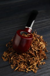 Photo of Smoking pipe and dry tobacco on black wooden table, closeup