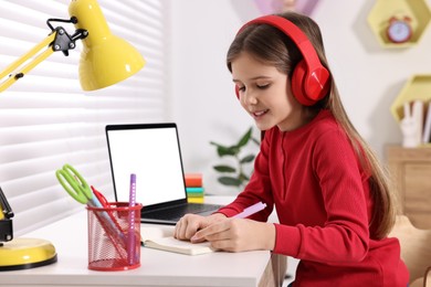 E-learning. Girl taking notes during online lesson at table indoors