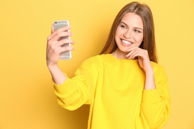 Young beautiful woman taking selfie against color background