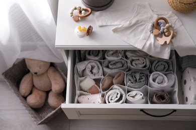 Photo of Modern open chest of drawers with baby clothes and accessories in room, above view