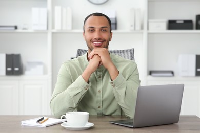 Photo of Handsome young man with laptop at table in office