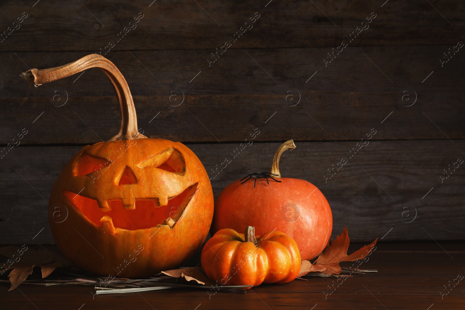 Photo of Halloween pumpkin head jack lantern and autumn decorations on table against wooden background with space for text