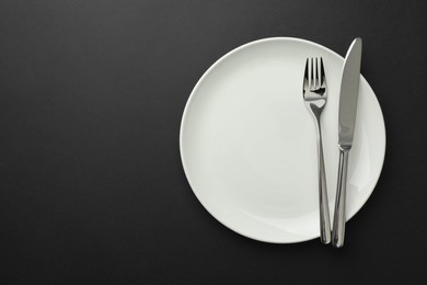 Photo of Clean plate, fork and knife on black table, top view. Space for text
