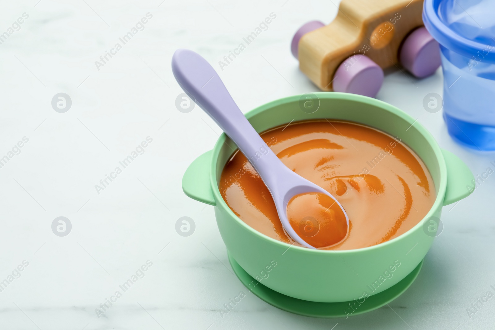 Photo of Bowl and spoon with tasty pureed baby food on white table, space for text