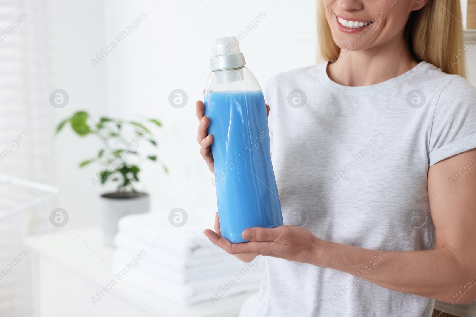 Photo of Woman holding fabric softener in bathroom, closeup. Space for text