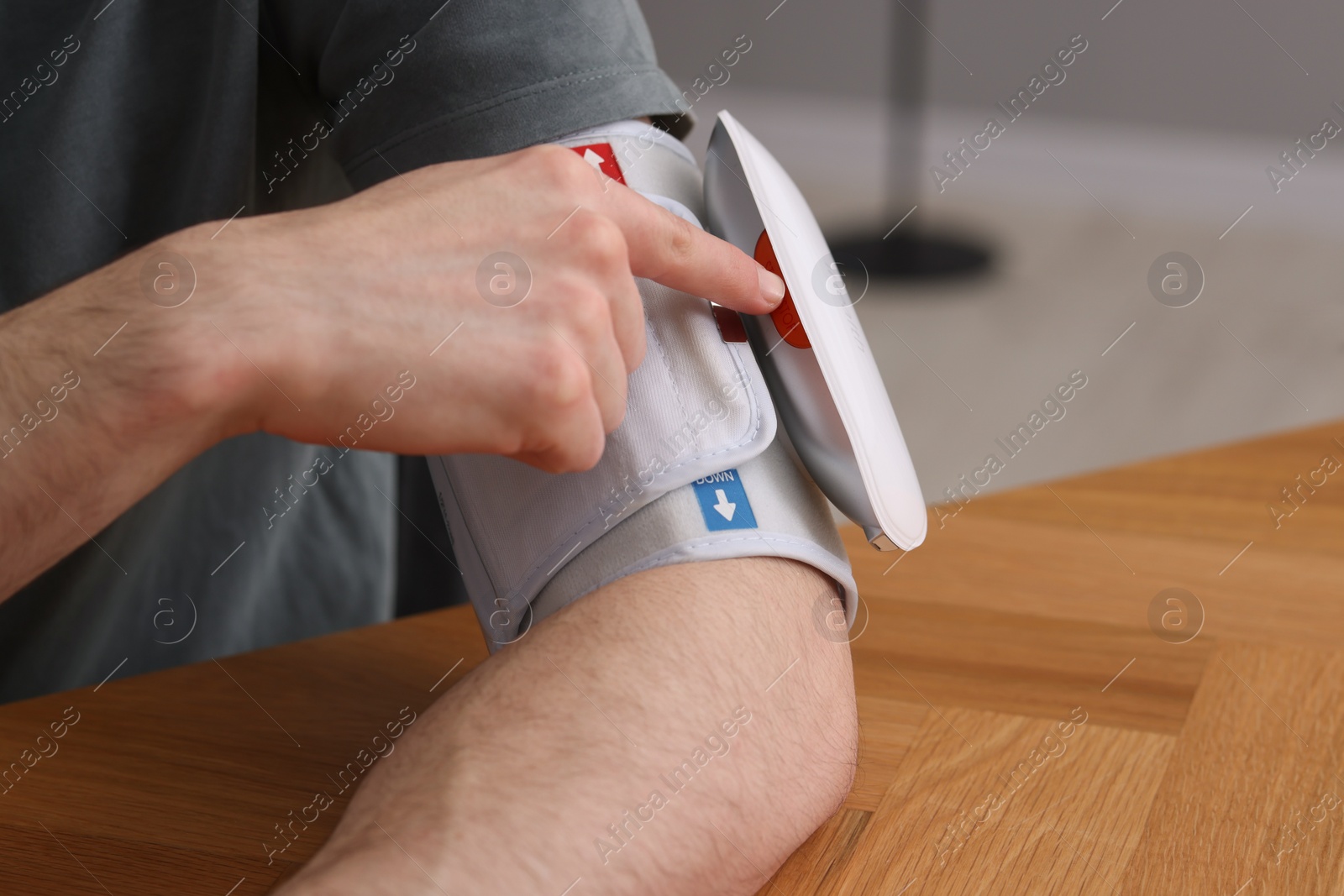 Photo of Man measuring his blood pressure with tonometer at wooden table indoors, closeup