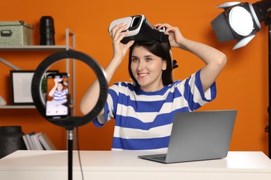 Smiling technology blogger wearing virtual reality headset while recording video at home