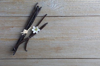 Photo of Vanilla pods and flower on wooden table, flat lay. Space for text