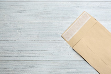 Photo of Kraft paper envelope on white wooden background, top view. Space for text