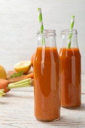 Photo of Bottles of fresh carrot juice on white wooden table
