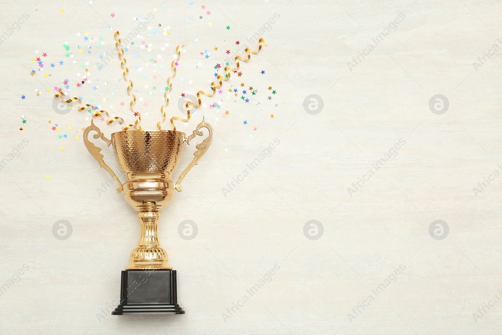 Photo of Golden trophy cup and streamers on wooden background, top view with space for text