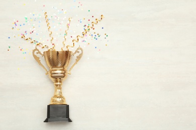 Golden trophy cup and streamers on wooden background, top view with space for text