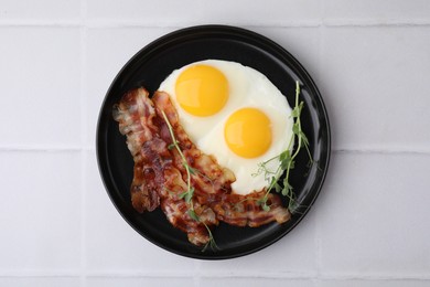 Fried eggs, bacon and microgreens on white tiled table, top view