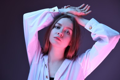 Photo of Fashionable portrait of beautiful young woman on purple background in neon lights