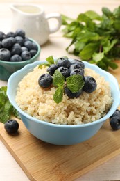 Photo of Tasty quinoa porridge with blueberries and mint in bowl on light table