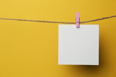 Photo of Wooden clothespin with blank notepaper on twine against yellow background. Space for text