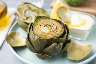 Photo of Delicious cooked artichokes with tasty sauce on plate, closeup
