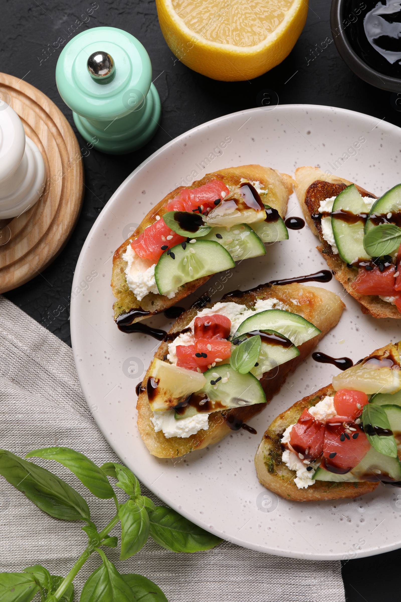 Photo of Delicious bruschettas with balsamic vinegar, toppings and spices on dark textured table, flat lay