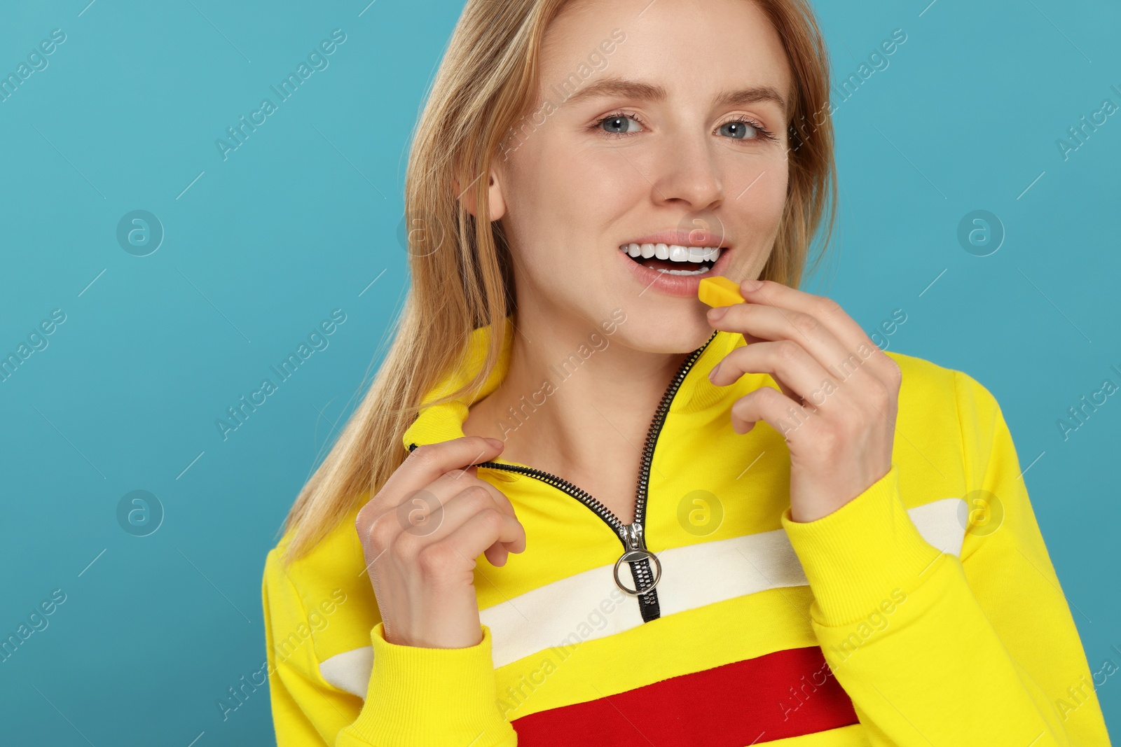 Photo of Happy young woman putting bubble gum into mouth on light blue background