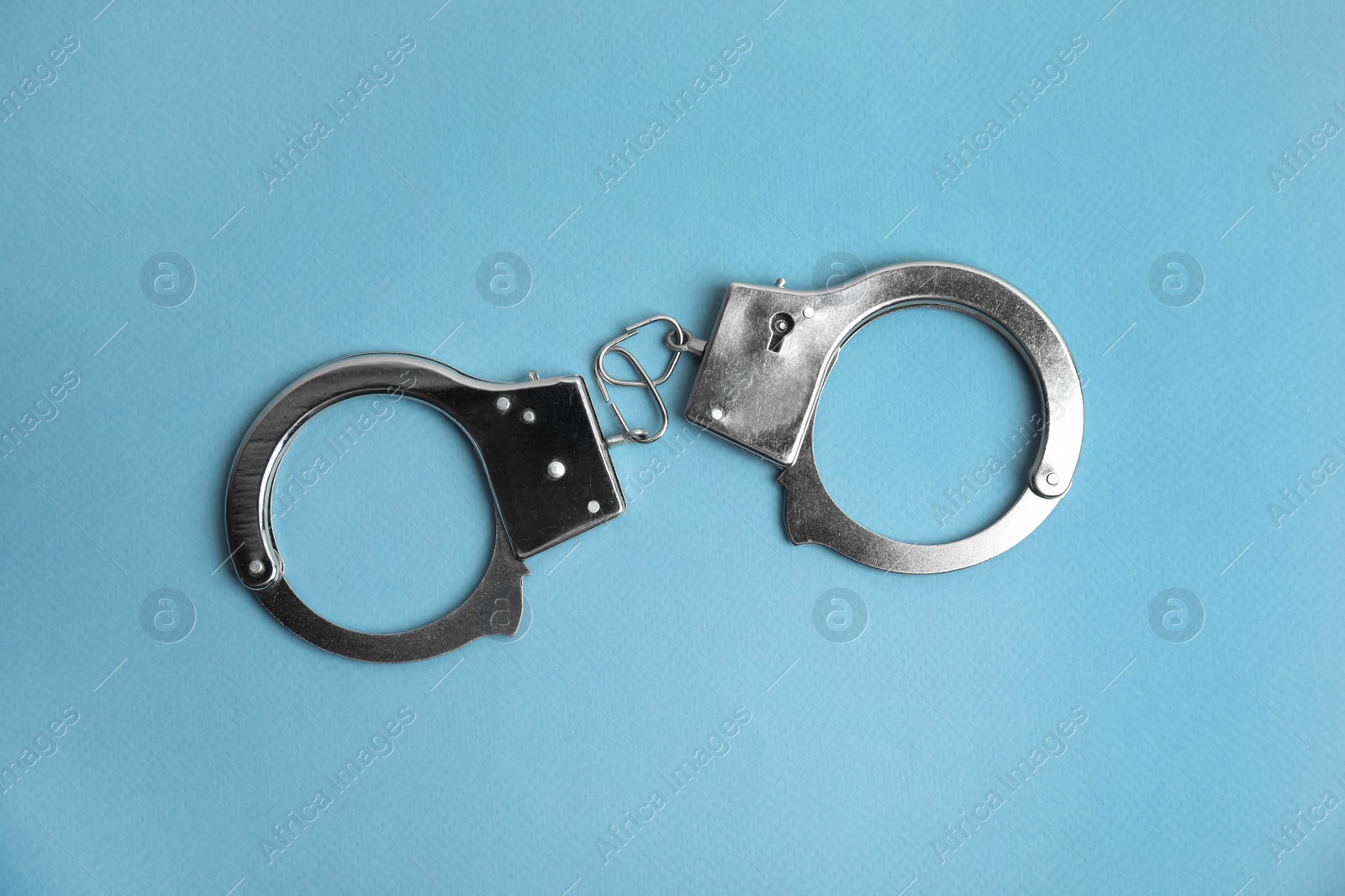 Photo of Classic chain handcuffs on light blue background, top view