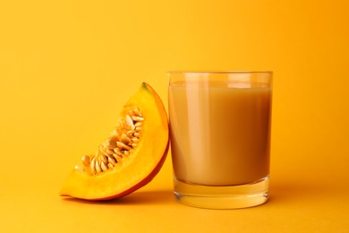 Tasty pumpkin juice in glass and cut pumpkin on orange background