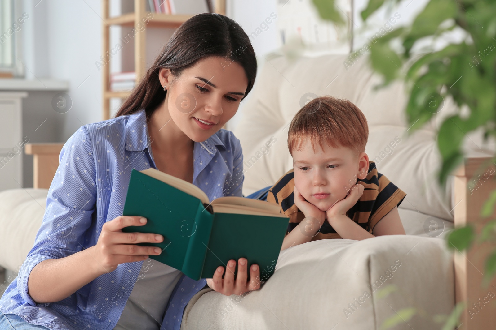 Photo of Mother reading book with her son in living room at home