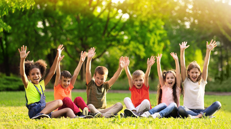 Image of School holidays. Group of happy children sitting on green grass outdoors