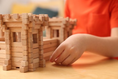 Photo of Little boy playing with wooden fortress at table in room, closeup. Child's toy