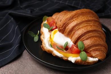 Tasty croissant with fried egg, tomato and microgreens on brown textured table, closeup