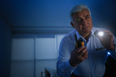 Photo of Professional security guard with portable radio set and flashlight in dark room