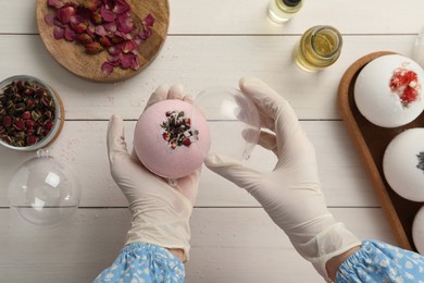 Photo of Woman in gloves with self made bath bomb at white table, top view
