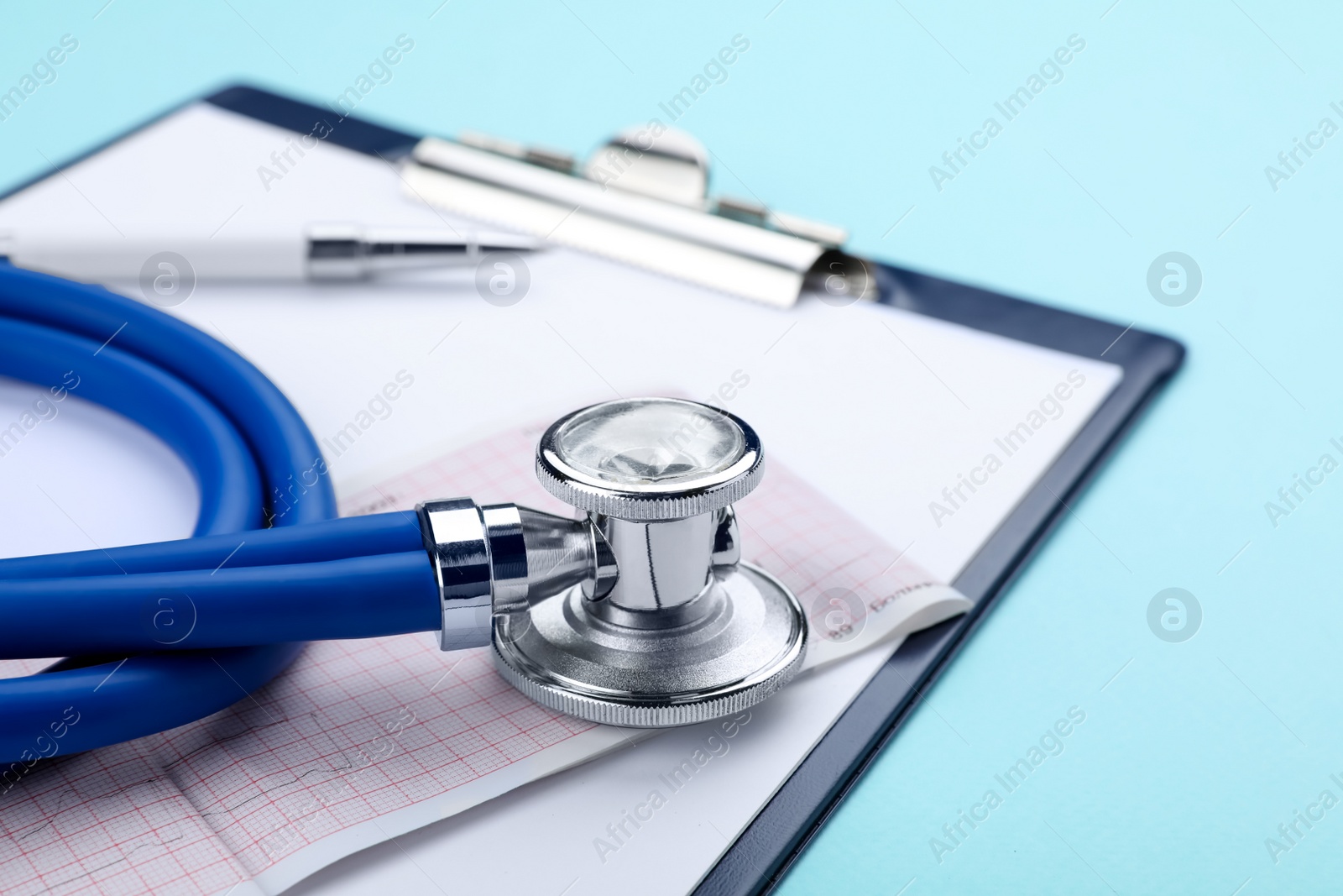 Photo of Clipboard with stethoscope and cardiogram on turquoise background, closeup