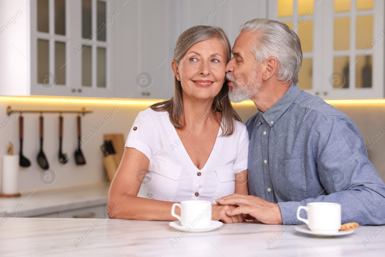Photo of Senior man kissing his beloved woman in kitchen, space for text