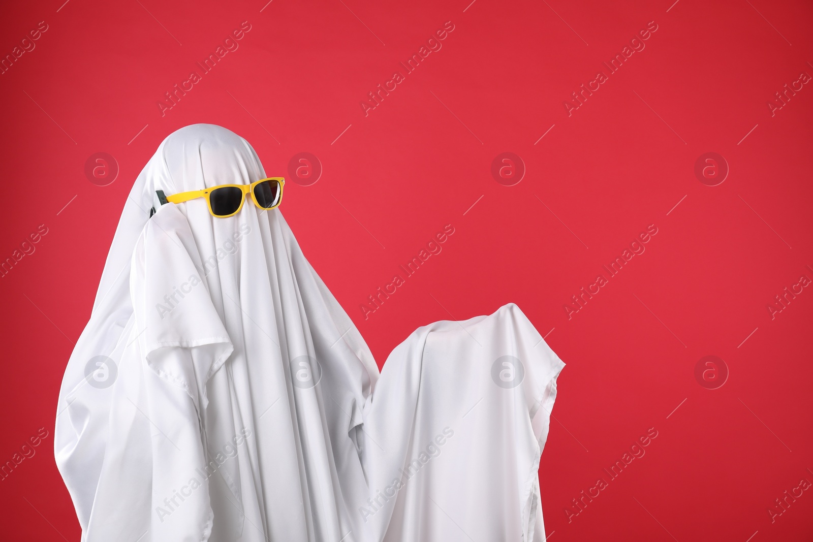 Photo of Person in ghost costume and sunglasses talking on smartphone against red background, space for text