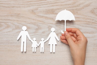 Woman holding umbrella near paper family cutout on white wooden background, top view. Insurance concept