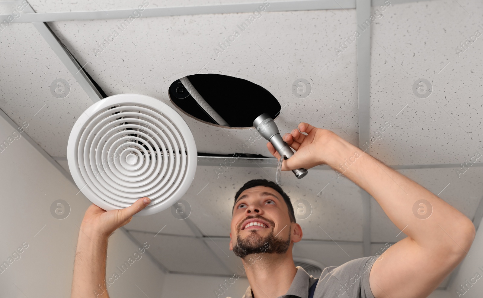 Photo of Repairman with flashlight fixing ventilation system indoors