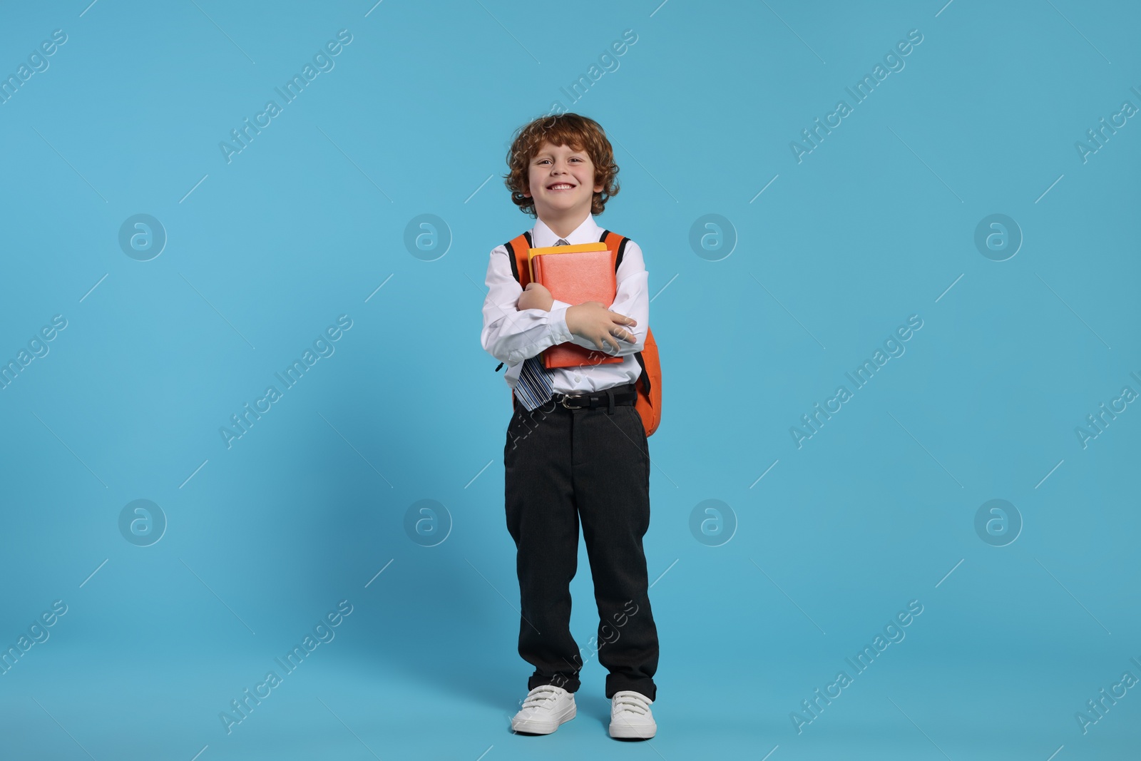 Photo of Happy schoolboy with backpack and books on light blue background